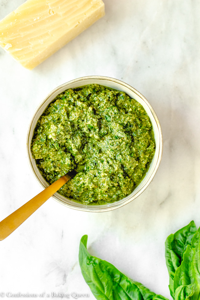 easy walnut pesto recipe served in a small bowl with a gold spoon on a white marble surface with a block of parmesan cheese and basil leaves