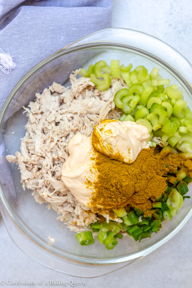 curried chicken salad recipe ingredients in a clear bowl before mixing on a white background with a grey linen
