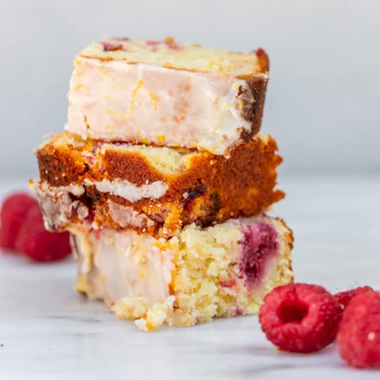 raspberry lemon loaf cake pieces stacked on top of each other with raspberries on a white surface