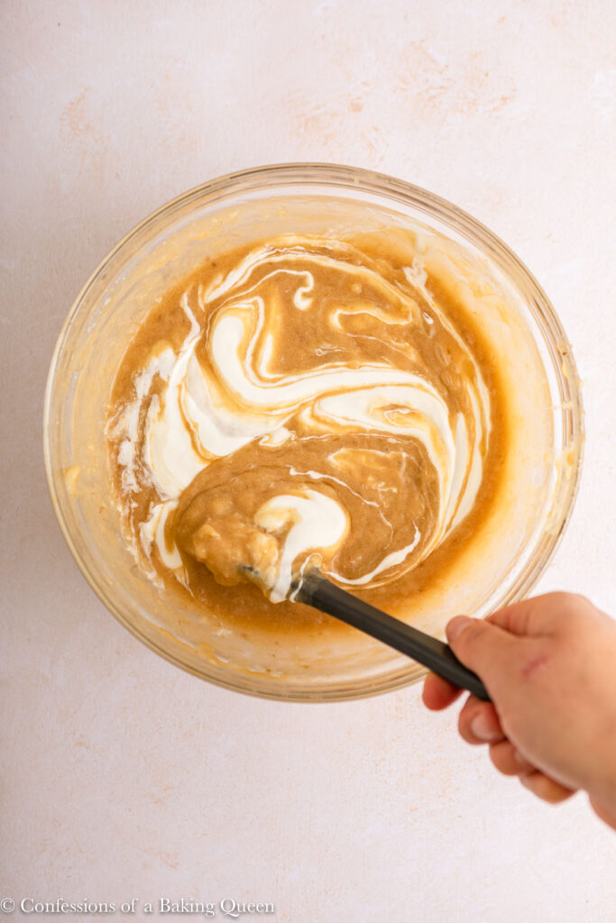 sour cream swirled into wet ingredients for banana bread on a light surface