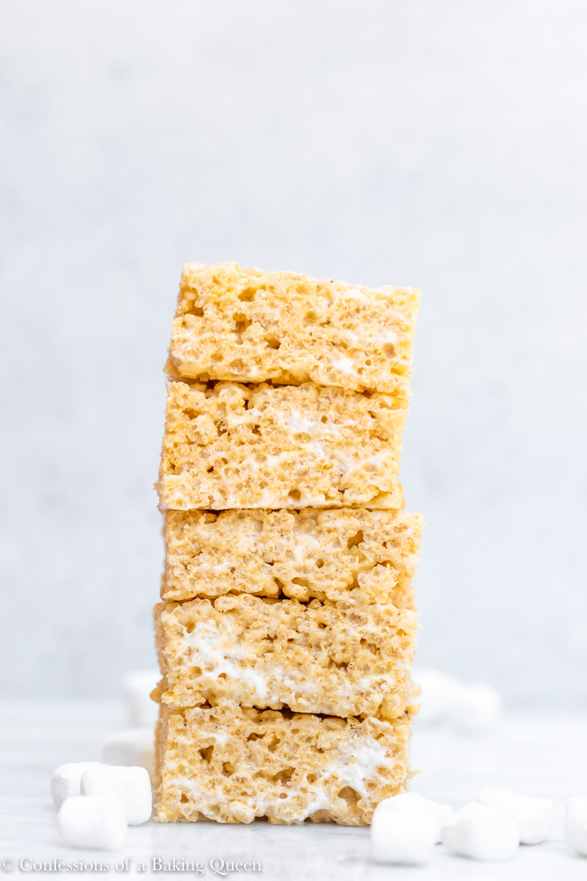 brown butter rice krispies stacked high with mini marshmallows next to the stack on a white marble surface