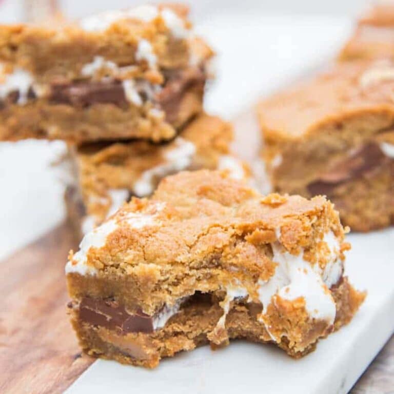 Cookie Butter S'mores Bars stacked in background with one bar with a bite taken out in the front on a marble surface