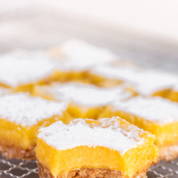 lemon bar with a bite missing on a wire rack with more lemon bars behind