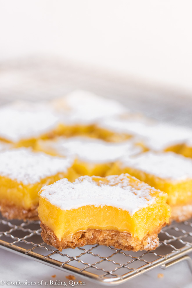 lemon bar with a bite missing on a wire rack with more lemon bars behind