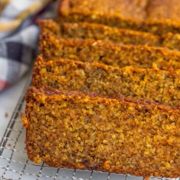 oat flour pumpkin bread sliced on a wire rack on a white background with an orange, yellow, and white linen