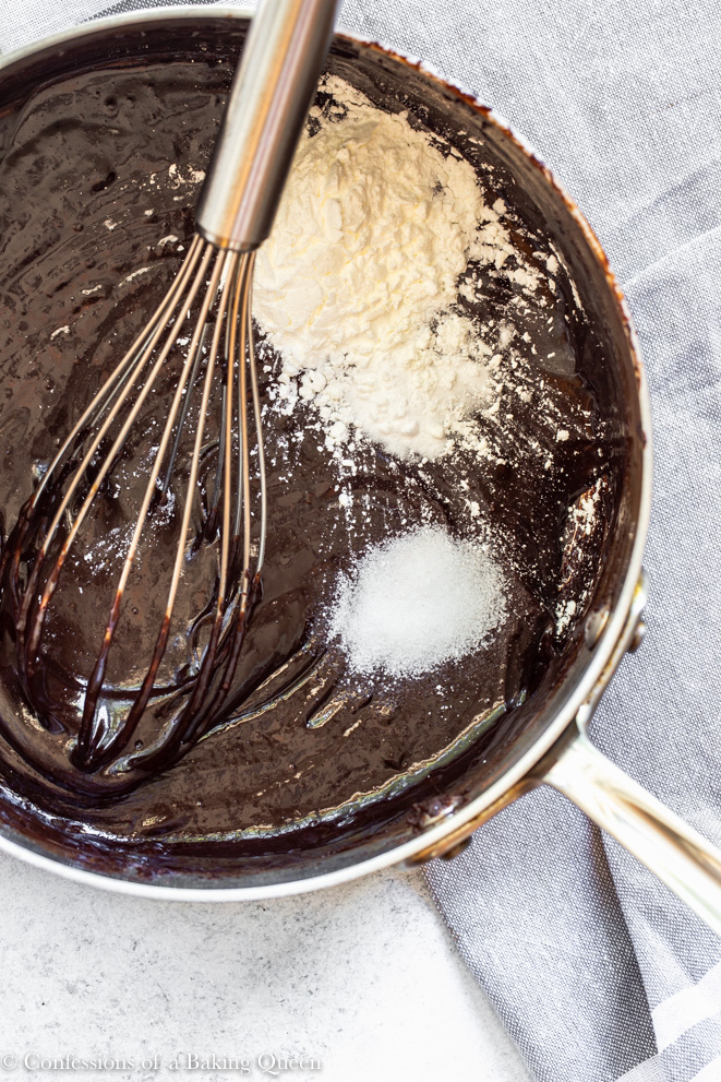 cornstarch, salt and baking soda added to peanut butter cup brownies in a stainless steel pan with a wire whisk on a light surface with a grey linen