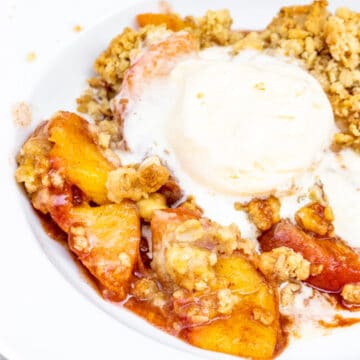 peach crumble recipe served with vanilla ice cream in a white bowl with a red and white checkered towel in the background
