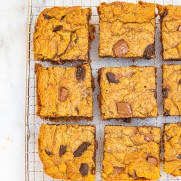 chocolate chunk blondies cut into squares cooling on a wire rack on a white marble surface