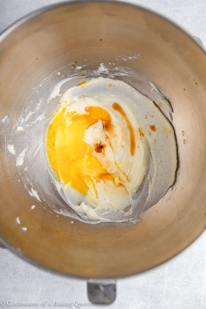 egg and vanilla added to cream cheese mixture in a metal bowl