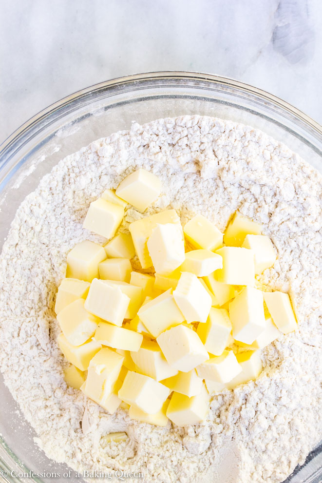 butter added to a bowl of flour for a pie crust recipe on a white marble surface