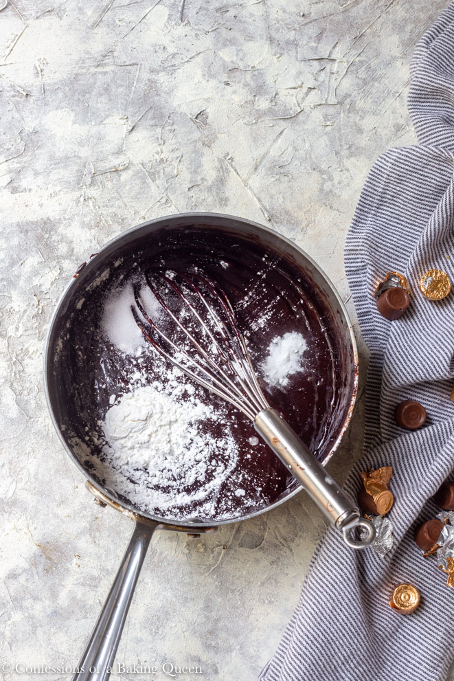 cornstarch, salt, and baking soda added to rolo brownie batter in a large saucepan on a grey surface with a blue stripped linen