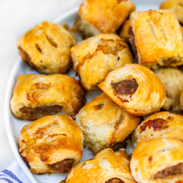 sausage rolls recipe served on a white plate on top of white and blue tea towel