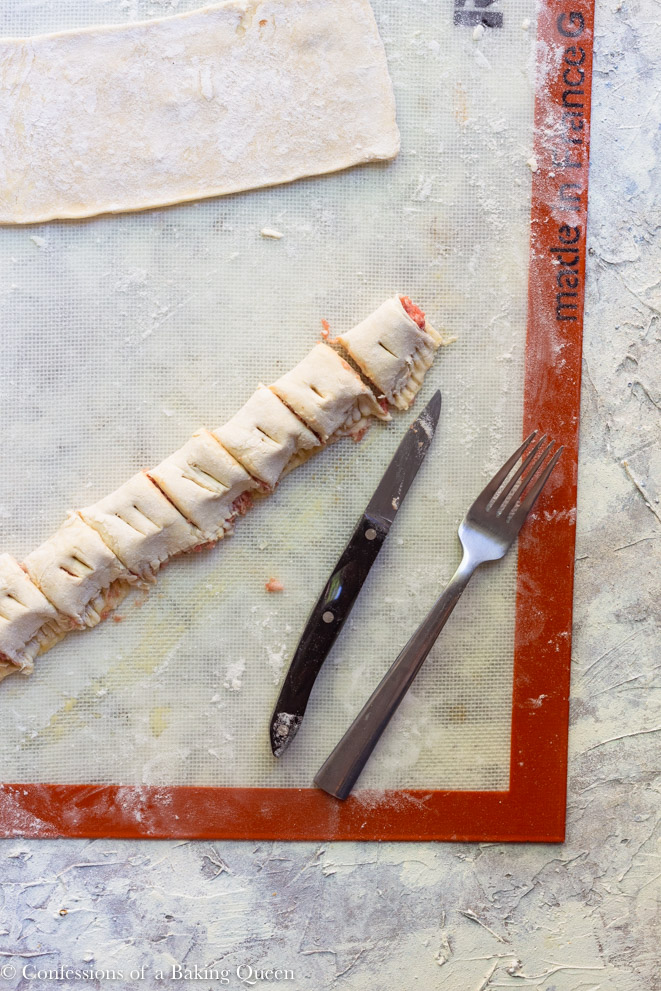 knife and fork on a work surface with cut and scored mini sausage rolls on a grey background