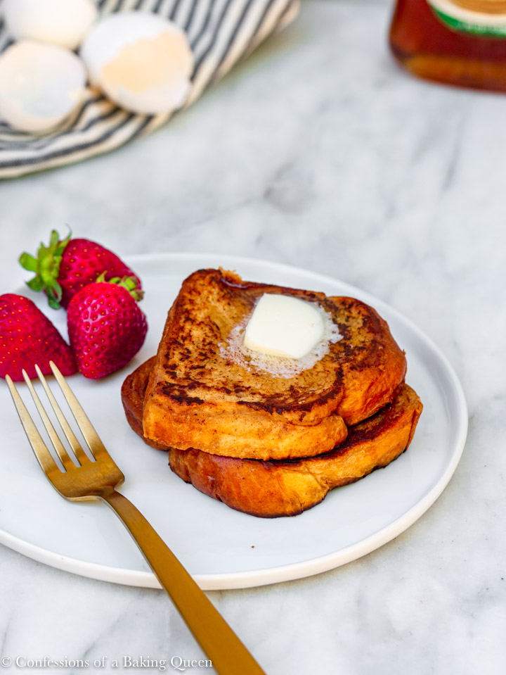 the best french toast stacked on a white plate with butter melting on top and strawberries