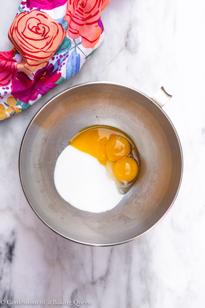 egg yolks and sugar in a metal mixing bowl on top of a marble counter for a How To Make Tiramisu