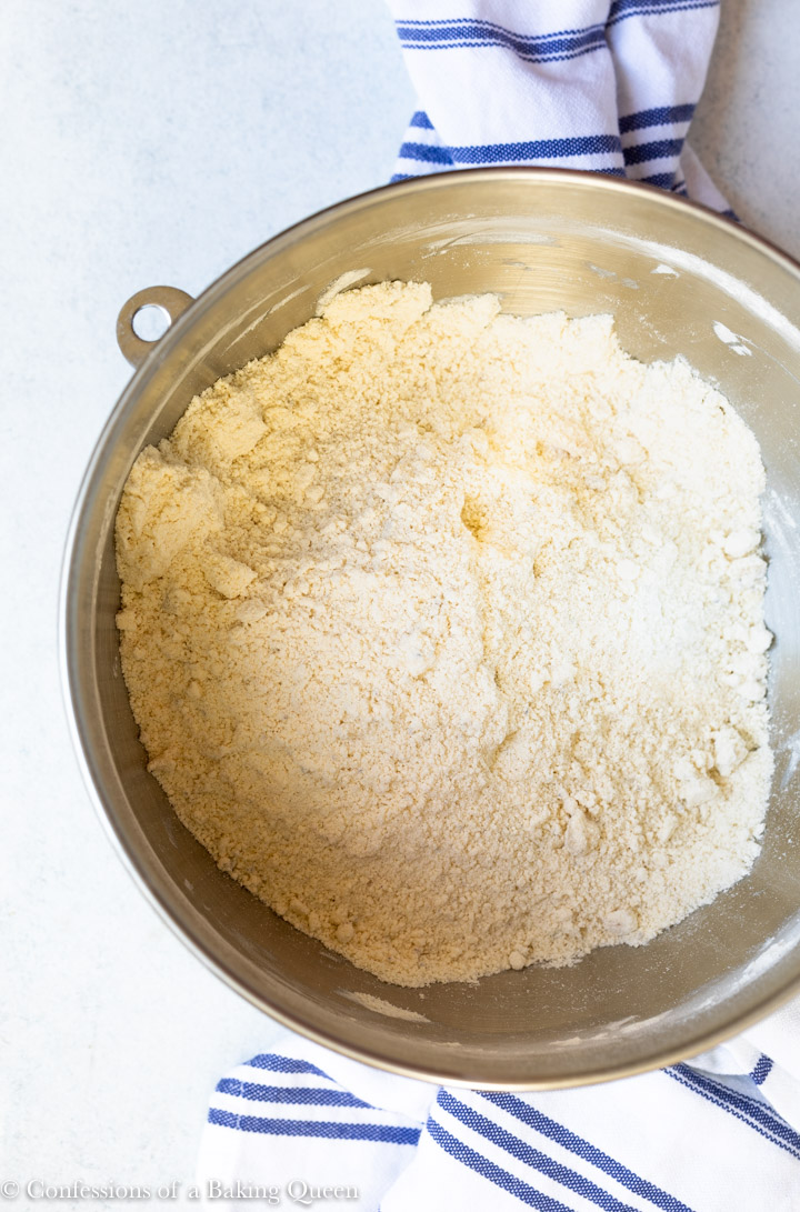 scone batter before the liquid in a large metal bowl on a white surface with a white and blue linen 