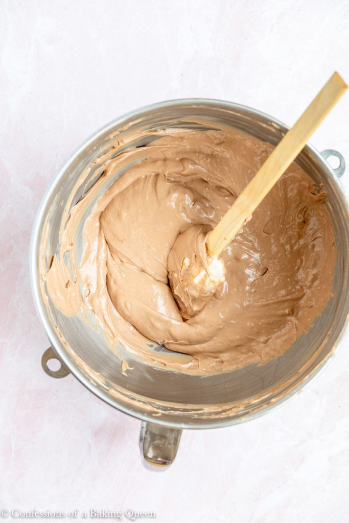 chocolate cheesecake batter in a metal mixing bowl with a wood spatula