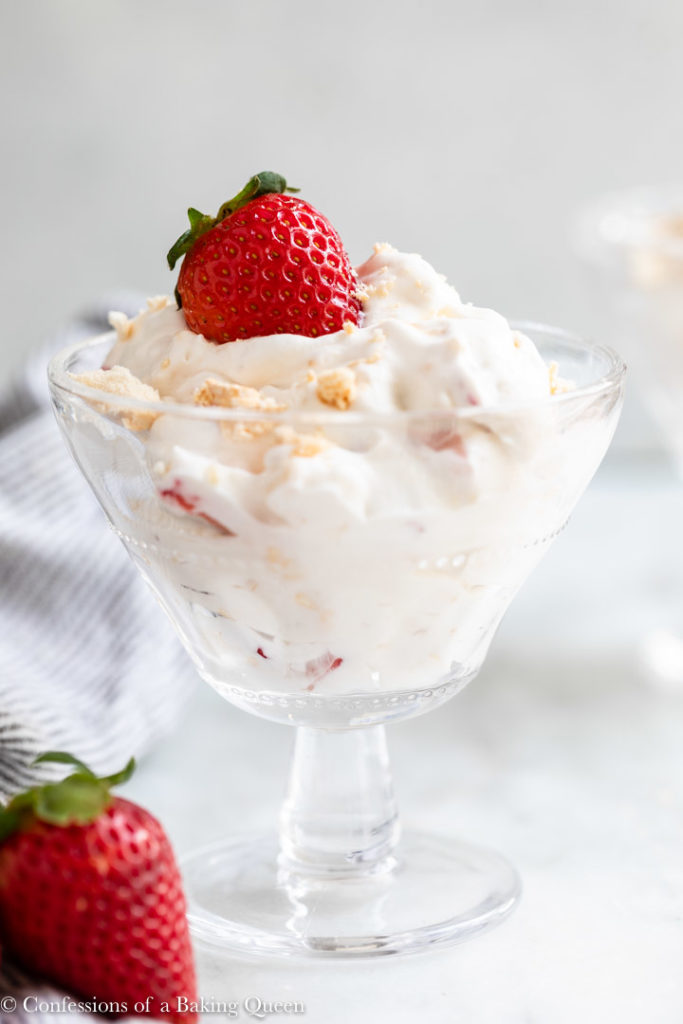 eton mess in a tall glass dish with a strawberry on top