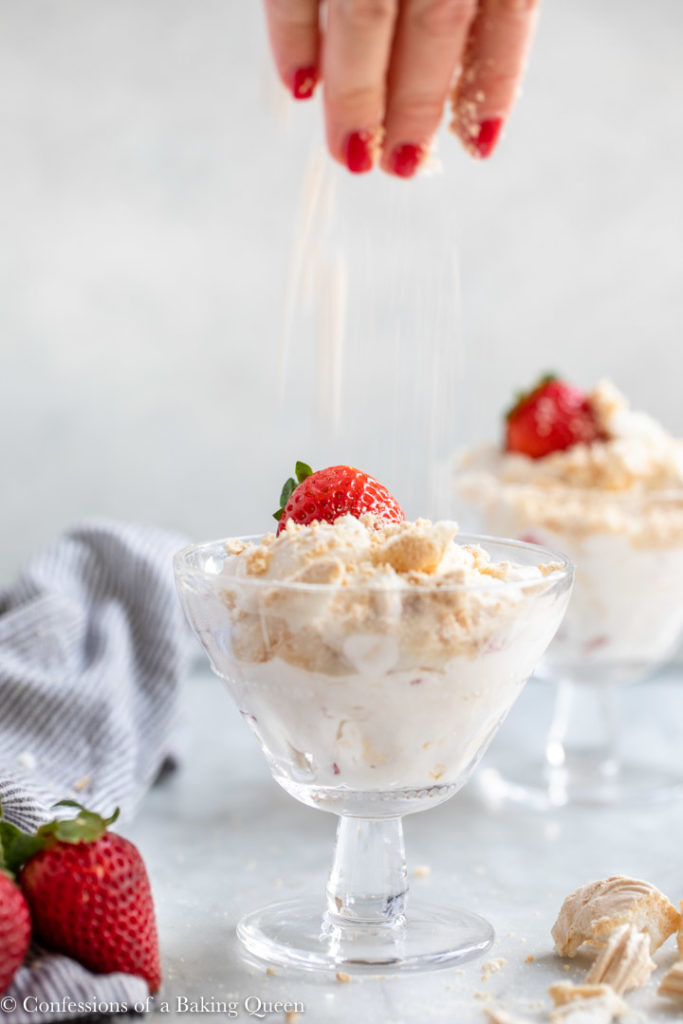 hand sprinkling crushed meringues on top of a glass full of eton mess