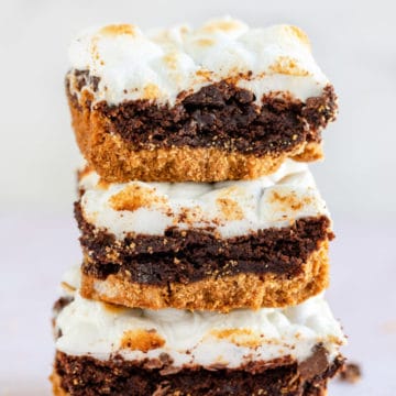 three s'mores brownies stacked on top of each other on a light pink surface
