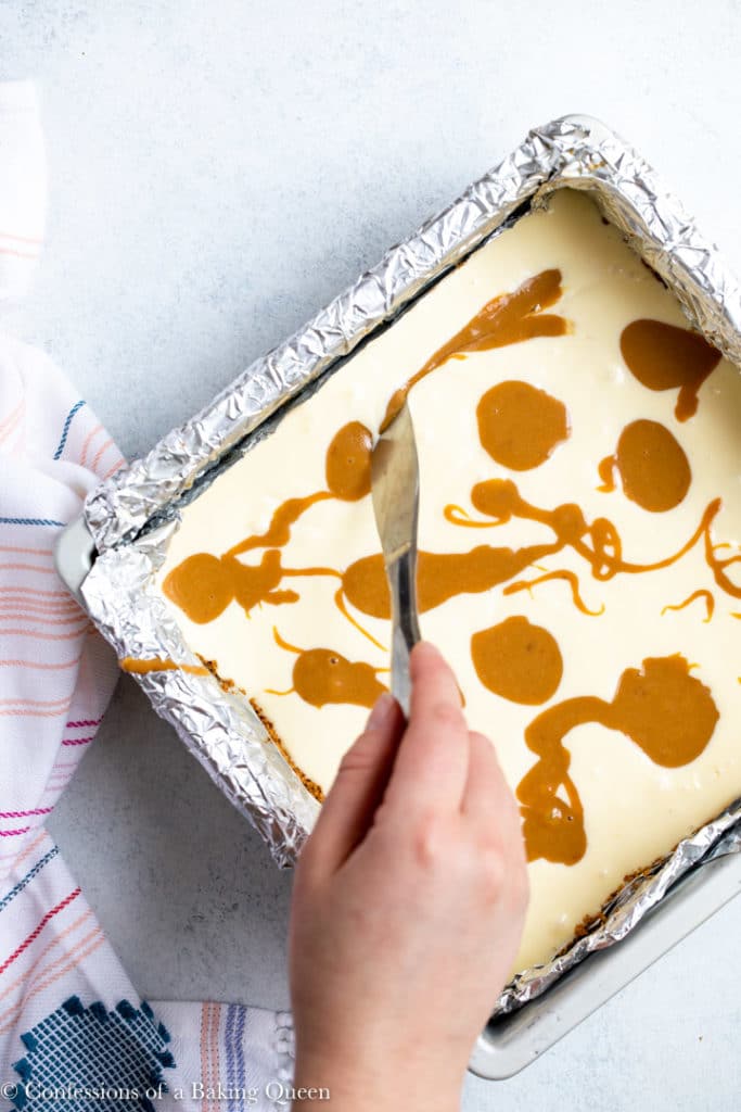 hand holding a knife swirling dulce de leche into cheesecake batter