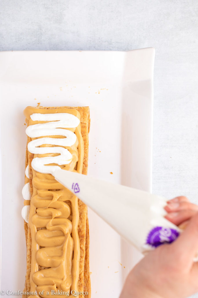 hand holding piping bag full of whipped cream, piping on to a millie feuille