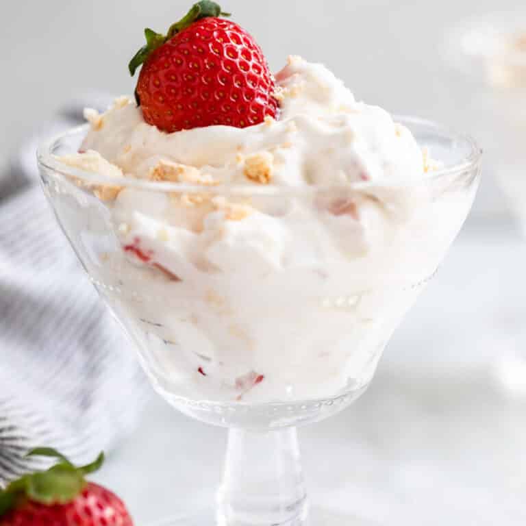 eton mess served in a tall glass dish with crushed meringues and strawberry on top