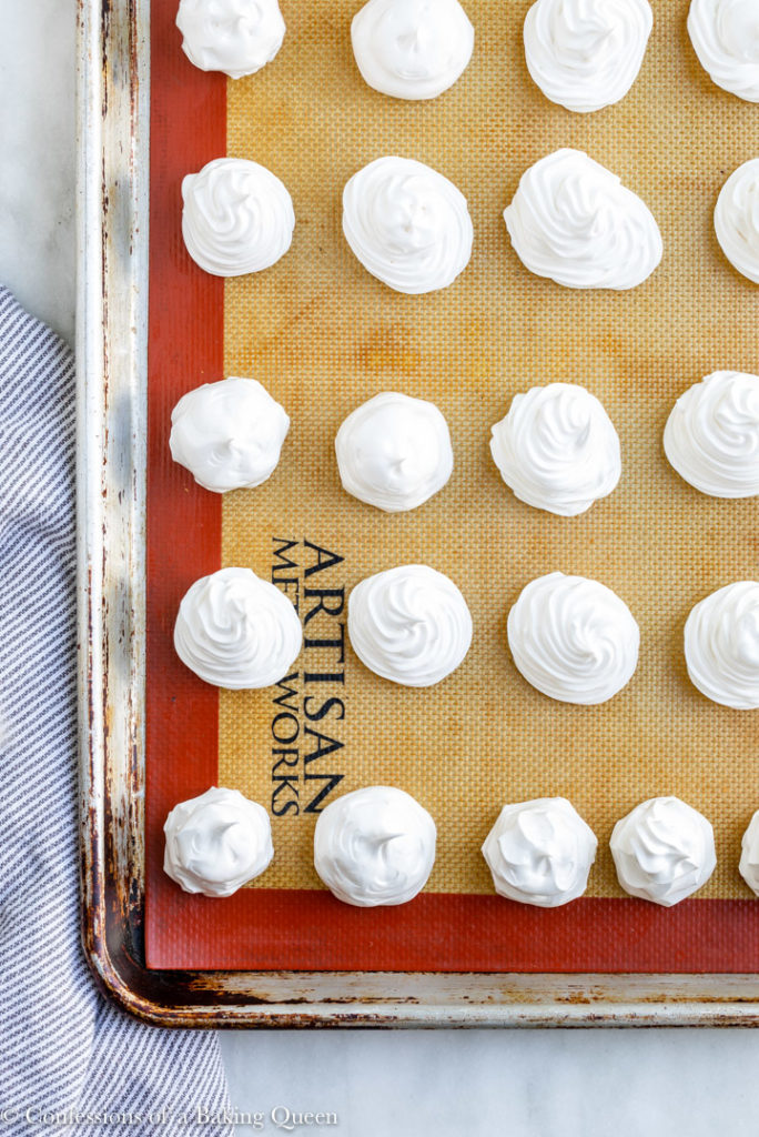 meringue cookies piped before baking on a silpat lined baking sheet  on a marble surface with a white and blue linen