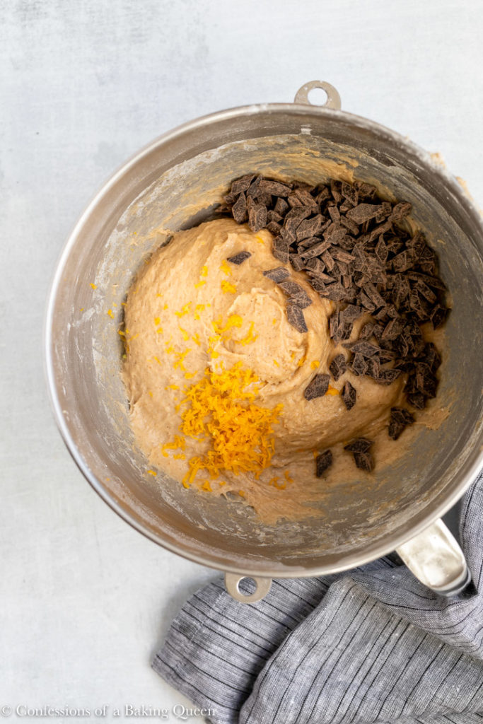 chocolate chunks and orange zest added to hot cross bun dough in a metal mixing bowl