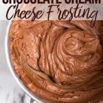 chocolate cream cheese frosting in a large metal mixing bowl on a white marble surface with a floral linen