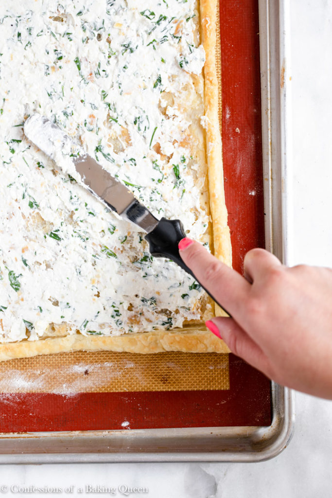 hand holding a spatula spreading feta spread on puff pastry