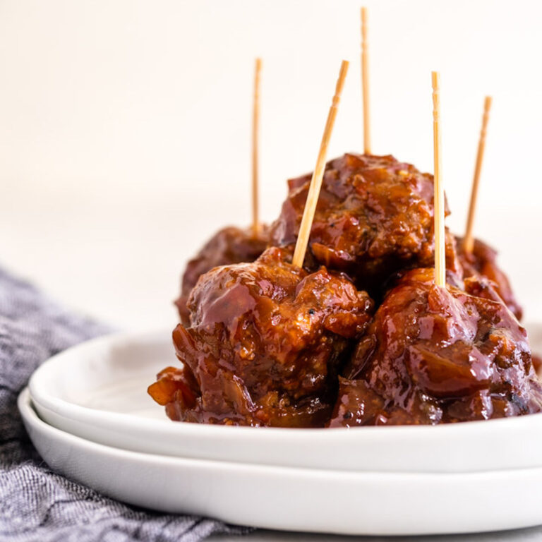 crockpot bbq meatballs with toothpicks sticking out on a white plate on a white plate with a blue linen