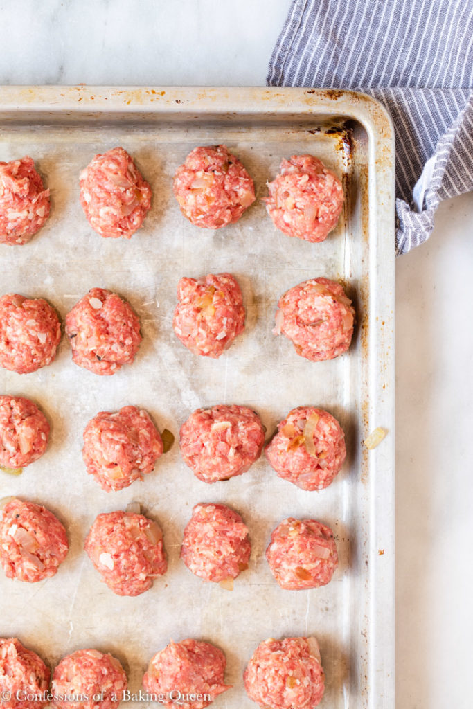 meatballs rolled out on a baking sheet on a white marble surface with a white and blue linen
