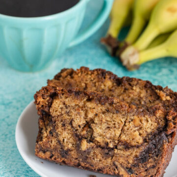 two slices of cinnamon swirl banana bread on a white plate next to a cup of coffee and bananas