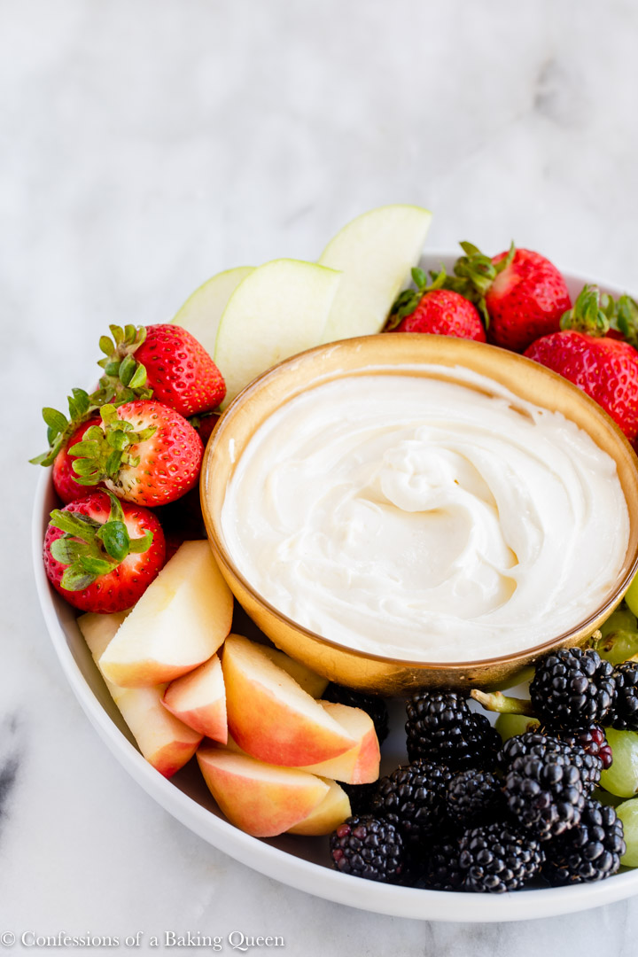 gold bowl full of cream cheese dip on a platter with fruit