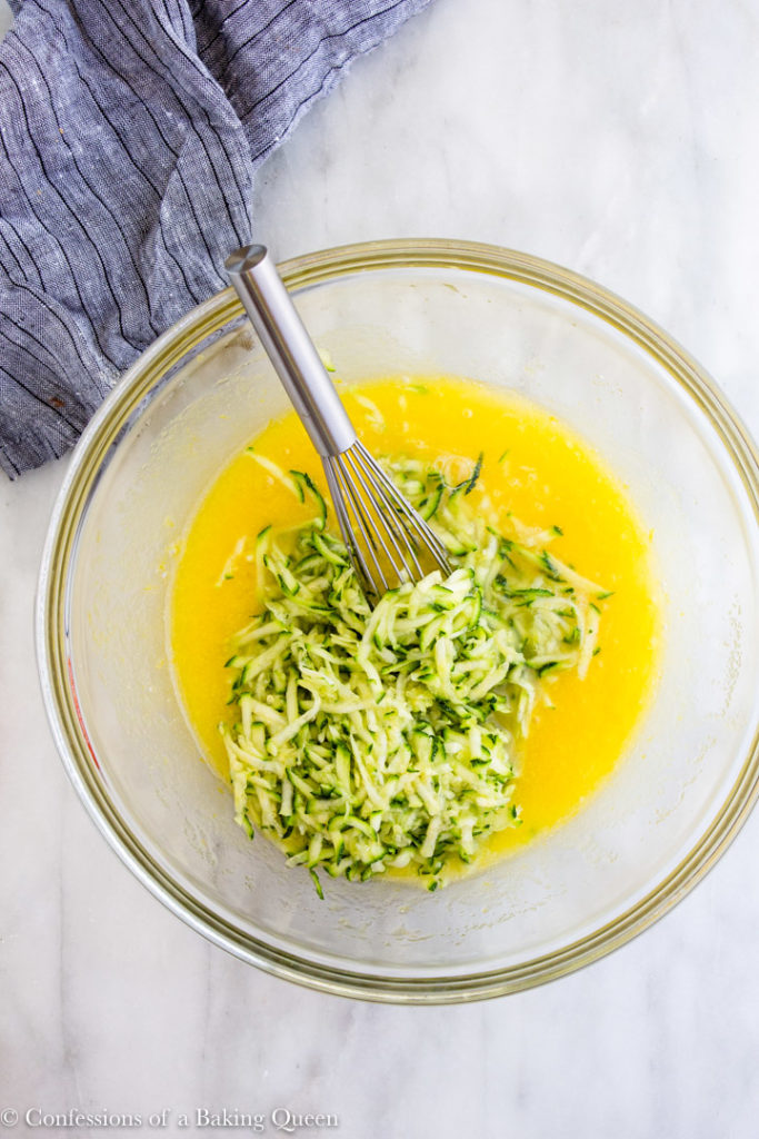 shredded zucchini added to a bowl of eggs, sugar and lemon zest