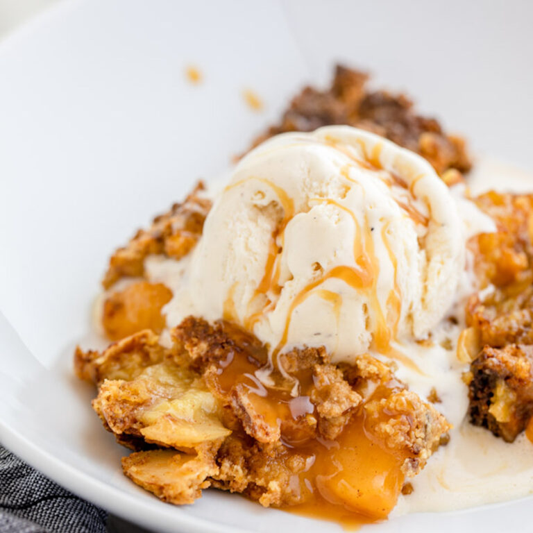 close up of peach dump cake on a white plate with ice cream