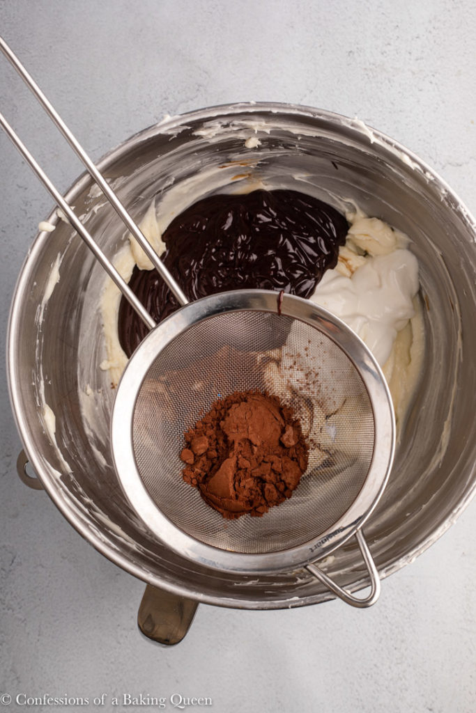cocoa powder in a sifter over a bowl of cheesecake batter