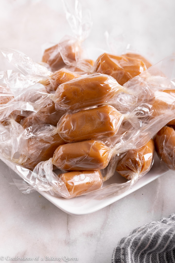 chewy caramels wrapped on a white plate on a white surface with a blue and white stripped linen