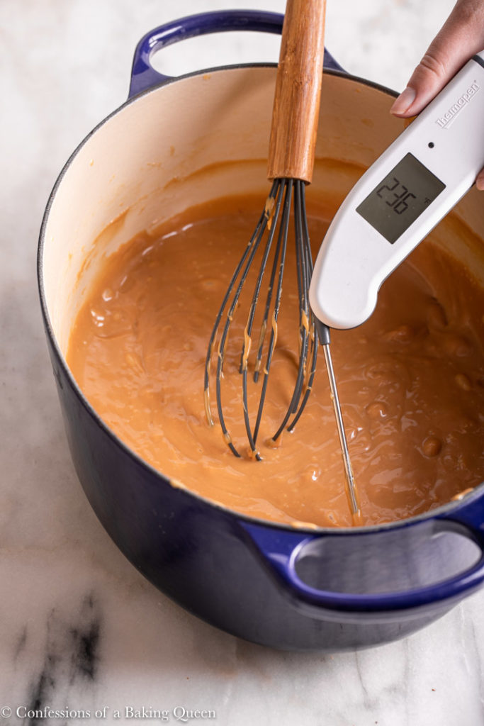thermometer checking temperature of chewy caramel mixture in a dutch oven with a whisk on a marble surface