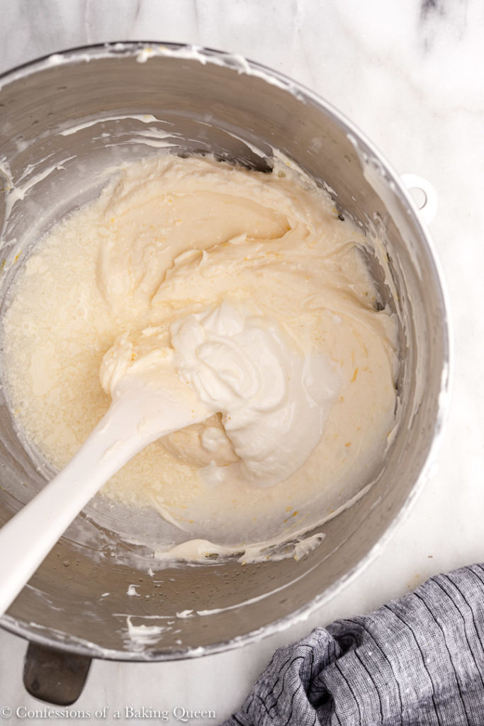 lemon juice,, sour cream, and heavy cream added to cheesecake batter in a metal mixing bowl