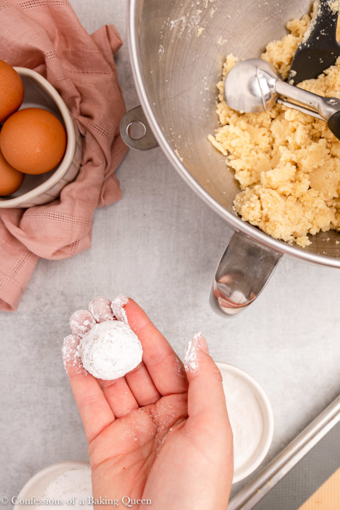 hand holding amaretti cookie ball rolled in powdered sugar