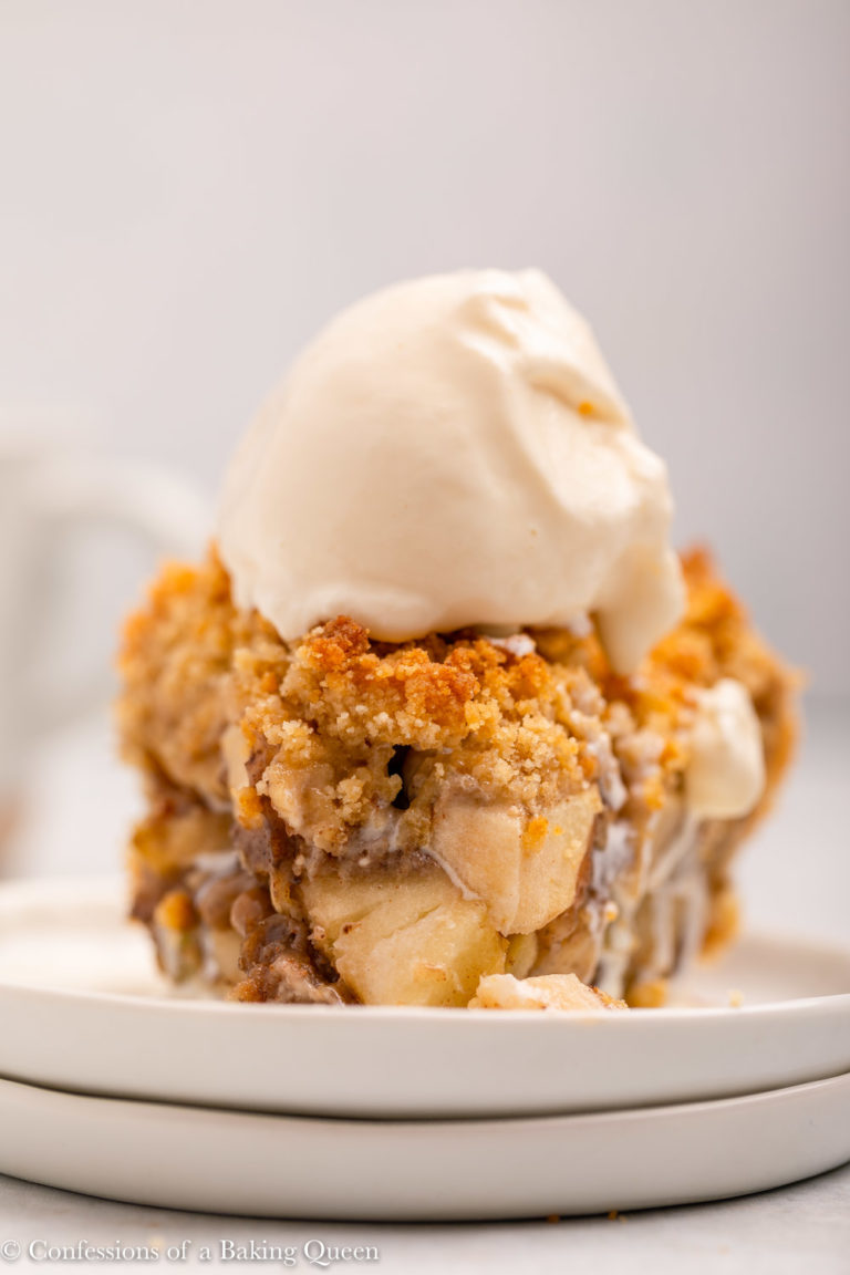 close up of a slice of dutch apple pie with ice cream on a white plate