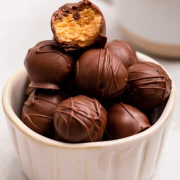 small bowl of peanut butter balls with one broken in half on top
