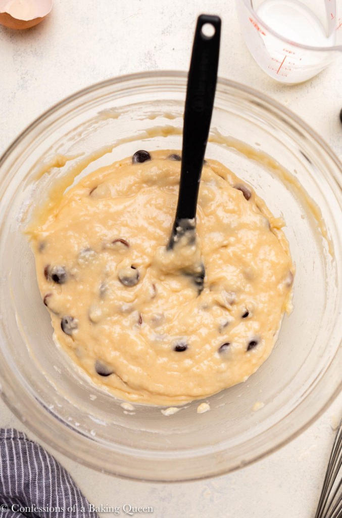 close up of chocolate chip muffin batter in a large glass bowl with a grey spatula