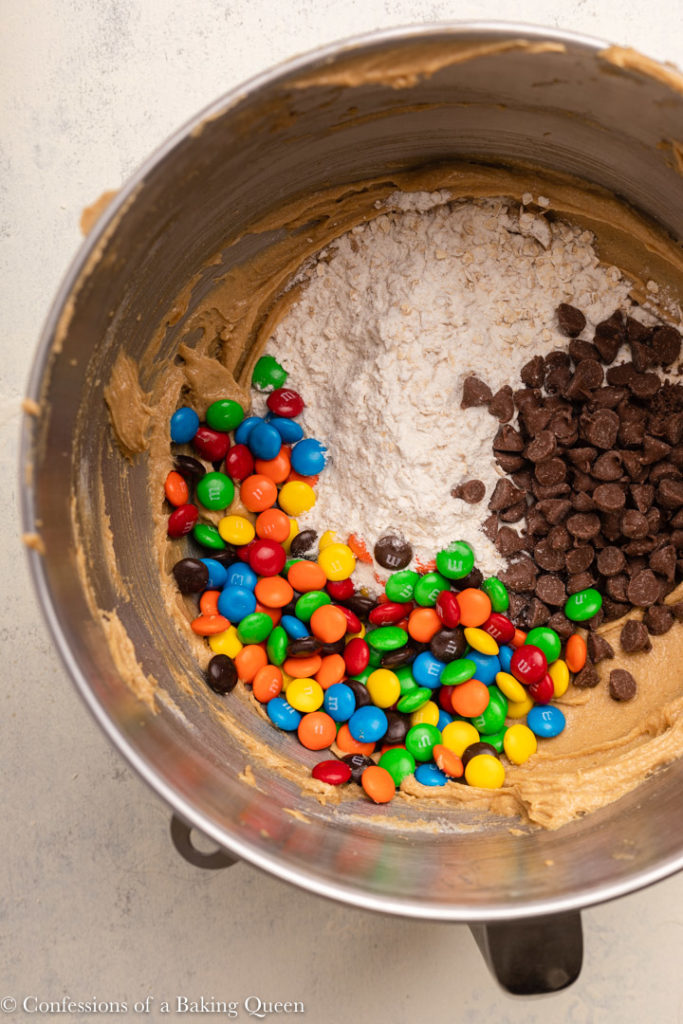 m&ms, chocolate chips, and dry ingredients added to wet ingredients in a metal mixing bowl