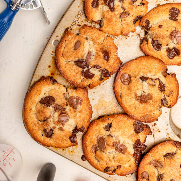 chocolate chip muffins baked in a muffin tin next to a whisk, cookie scoop and egg shell