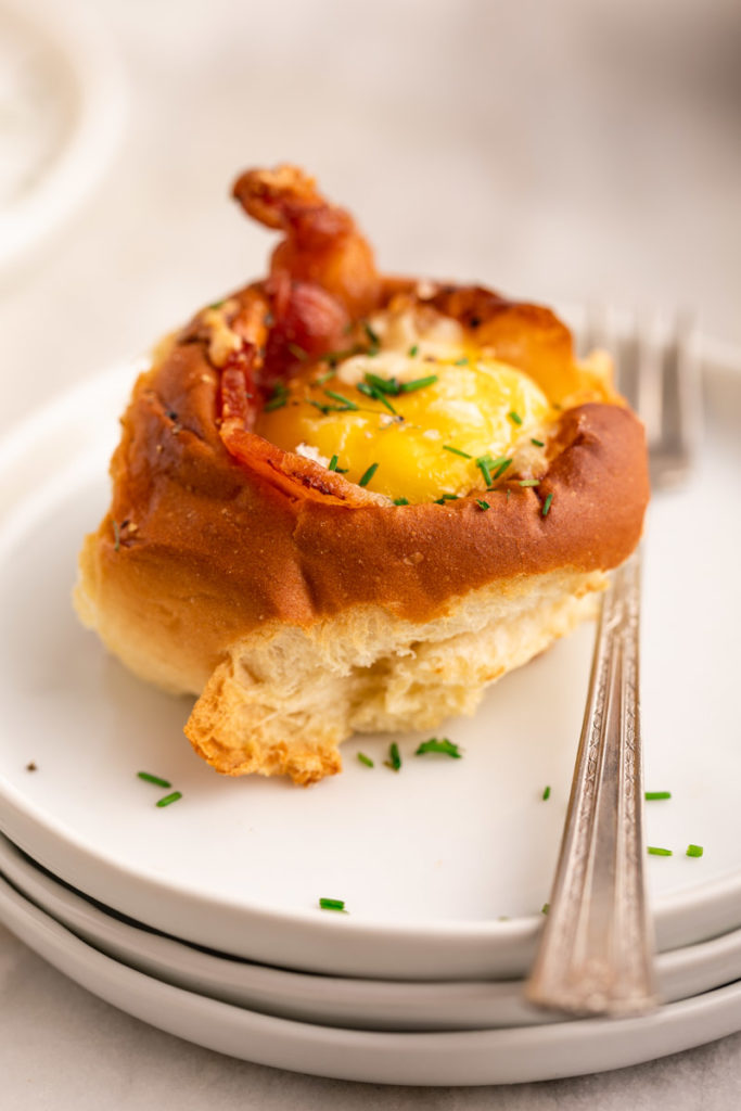 egg in a hole roll on a stack of white plates with a small fork 