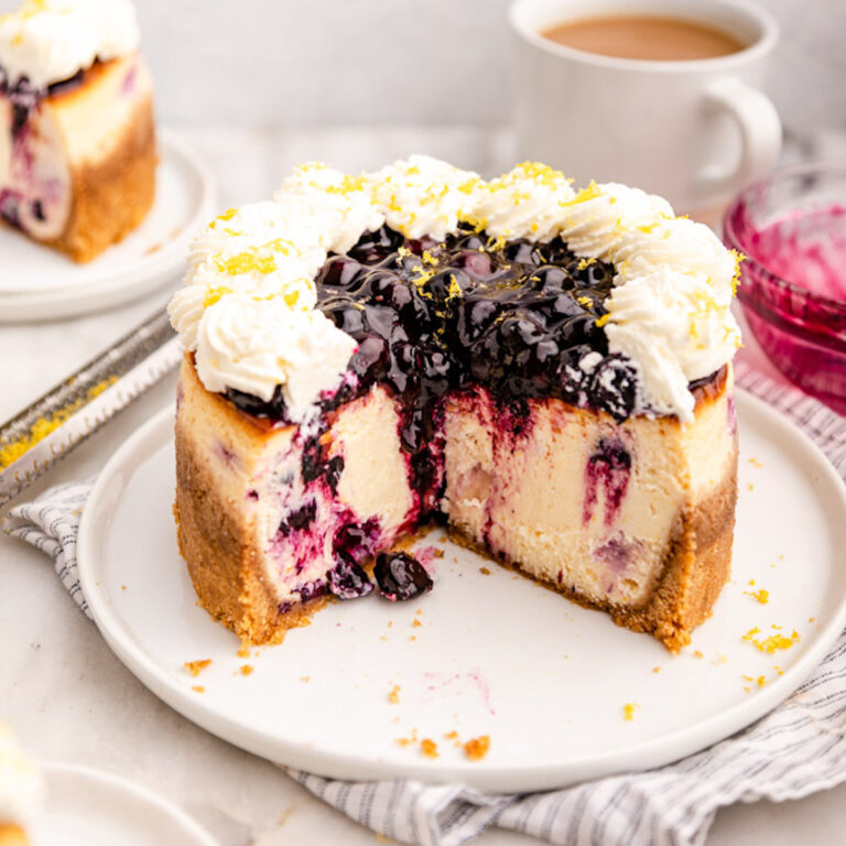 lemon blueberry cheesecake cut open on a plate next to a cup of tea and a slice of cheesecake