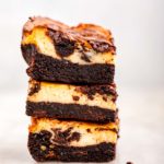 stack of three cheesecake brownies on a white marble surface